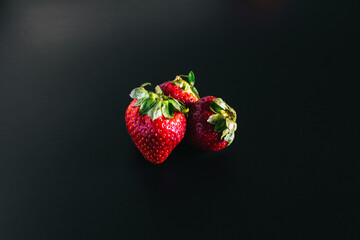 three juicy strawberries lie on a black background