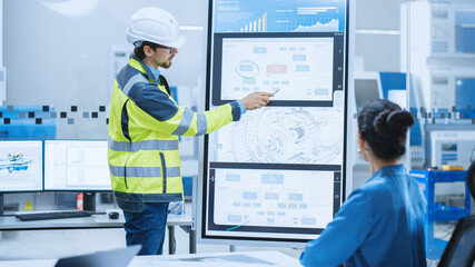 On a Meeting Chief Industrial Engineer Wearing Safety Jacket, and Hardhat Reports to a Group of...