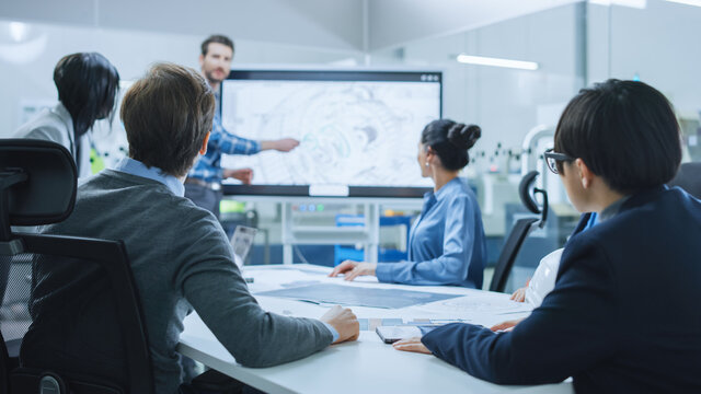 Modern Factory Office Meeting Room: Busy Diverse Team of Engineers, Managers and Investors Talking at Conference Table, Use Interactive TV, Analyze, Find Solutions, Debate and Discuss Engine Concept