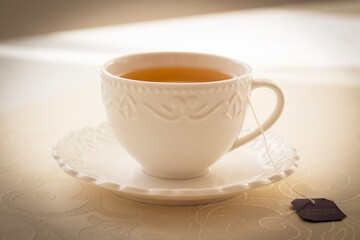 White festive cup with black tea and tea bag built on a beige tablecloth.