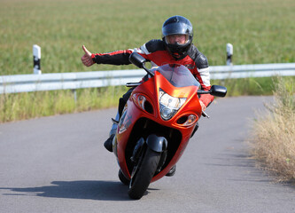 Fahrender Motorradfahrer zeigt mit ausgestrecktem Arm Daumen hoch