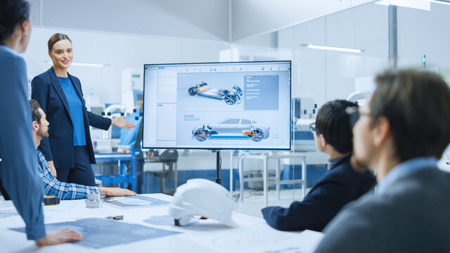 Confident Female Automotive Engineer Reports to Diverse Team of Specialists, Managers, Businesspeople and Investors Sitting at the Conference Table, She Shows TV with 3D Prototype of Electric Car