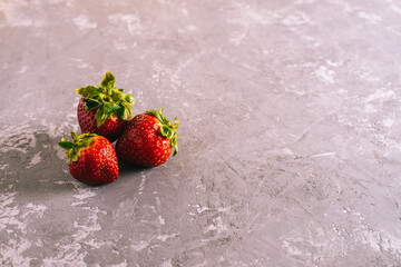 three fresh juicy strawberries lie on a concrete background.