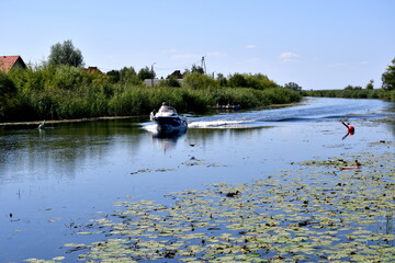 A view of a single boat swimming through a vast yet shallow lake full of reeds water lilies and other plants seen next to the Polish sea on a cloudless summer day during a hike