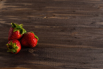three fresh juicy strawberries lie on an old table from a dark wood background.