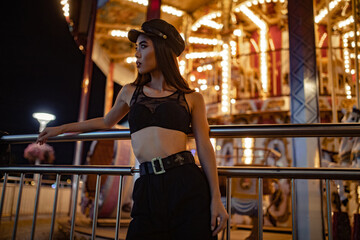 Fototapeta na wymiar Woman poses in night city near carousel against lights background.