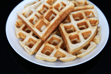 Belgian waffles in white plate on black glass table. Healthy breakfast, pieces of freshly baked classic wafer