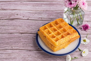 The waffle (or Honeycomb dessert) is placed on a white plate with flowers on a wooden table. Top view with space for text. Concept of dessert and relaxation