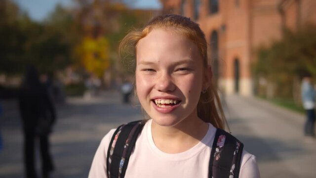 Close up portrait of happy laughing redhead schoolgirl standing outdoors
