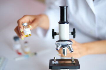 close-up photo of microscope for making medical research, female hand holding bottle with vaccine