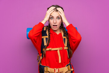 Young mountaineer girl with a big backpack over isolated purple background with surprise facial expression