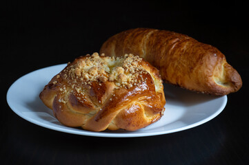 Two sweet bread on white plate with black wooden background