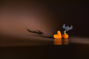 Halloween dark background with a contour light and shadow of heart, mini pumpkin and flying bat. Concept of art Halloween party. Copy space. Banner.