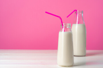 Two glass bottles of milk or milkshake against pink background