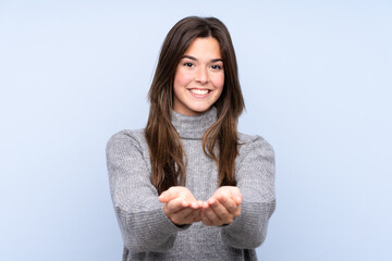 Teenager Brazilian girl over isolated blue background holding copyspace imaginary on the palm to...