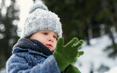 Front view of small child standing in snow, holiday in winter nature.