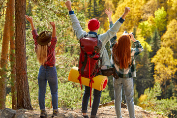 rear view on three travellers on mountains with hands up, happy man and women enjoy view on forests, autumn