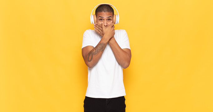 young black man covering mouth with hands with a shocked, surprised expression, keeping a secret or saying oops