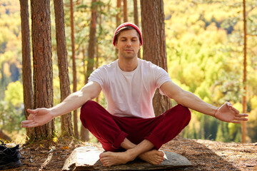Naklejka na ściany i meble young caucasian male sits in yoga pose on the mountain, male lead healthy lifestyle, keep calm, meditating, practive yoga exercises