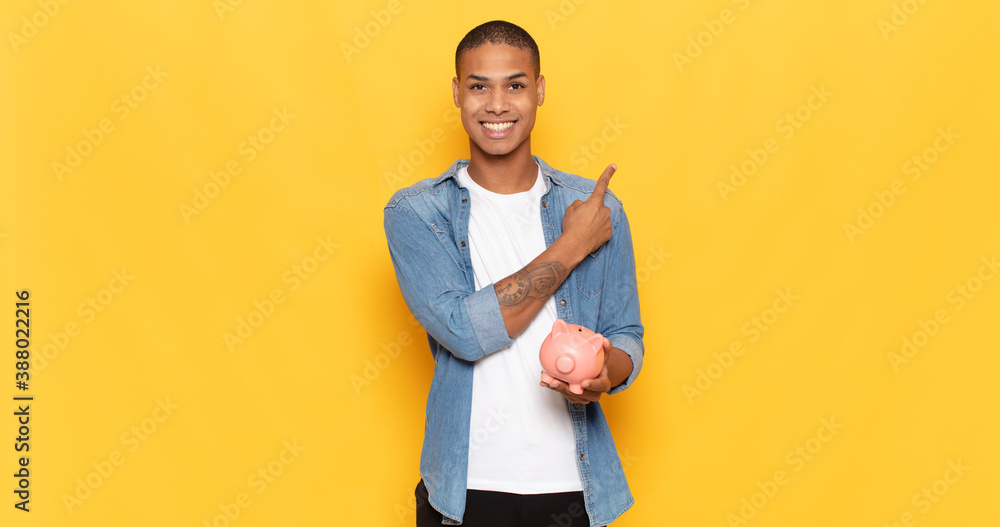 Sticker young black man smiling cheerfully, feeling happy and pointing to the side and upwards, showing object in copy space