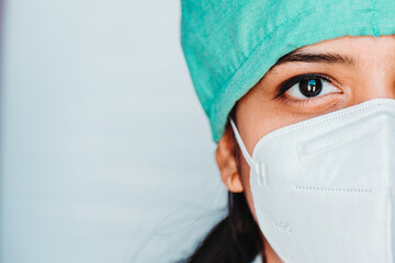 Close up portrait of half face of  young Indian female surgeon doctor in Emergency room wearing mask and cap during corona virus pandemic