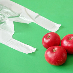 many red apples on paper bag vs polyethylene bag on green background, green grocery concept, zero...