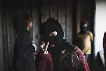 Girl with mask from teenagers gang standing indoors in abandoned building, showing middle finger.