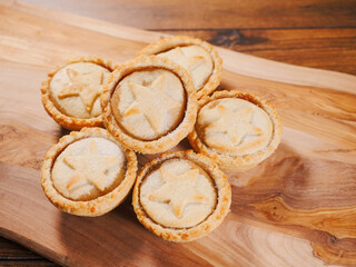 Stack of mince pies on a wooden board and table. Classic Christmas pastry product