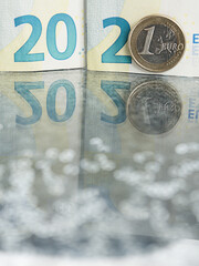 2021 sign made from 20 euro bank note and one euro coin on reflective surface with glitter bokeh.
