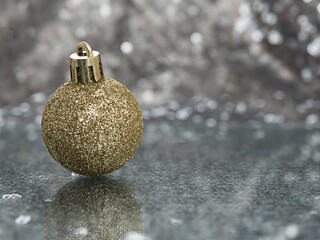One golden decoration ball on a reflective surface. Silver bokeh background. Christmas theme...