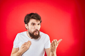 Emotional bearded man gestures with his hands in a white T-shirt aggression discontent red...