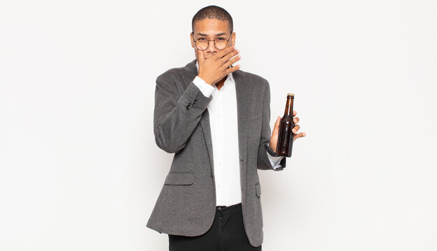 young black man covering mouth with hands with a shocked, surprised expression, keeping a secret or saying oops