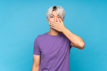 Young asian man over isolated blue background covering mouth with hands