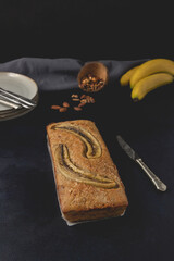 Banana nut bread loaf isolated on the dark background. Banana bread ingredients. Homemade delicious pastries. Front view.