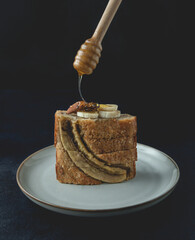 Slices of banana nut bread loaf with honey on top placed on the plate. An appetizing, soft bread texture, with crushed nut and honey aroma. Front view, close up.