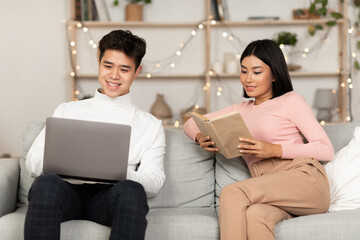 Fototapeta na wymiar Couple Relaxing Enjoying Weekend Reading Book And Using Laptop Indoor