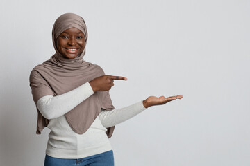 Smiling Black Muslim Lady In Hijab Pointing Finger At Her Open Palm