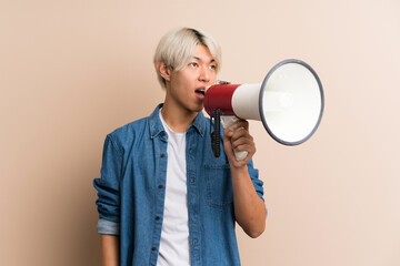 Young asian man over isolated background shouting through a megaphone