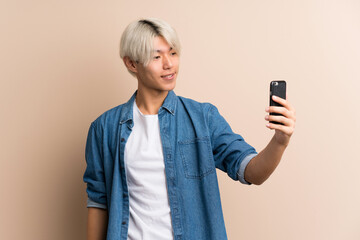Young asian man over isolated background taking a selfie with the mobile