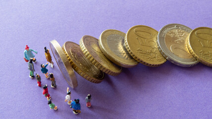Group of miniature people standing in front of falling row of euro coins on violet background from...
