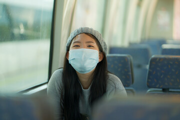 lifestyle portrait of young attractive and pretty Asian woman wearing mask in railcar traveling in...