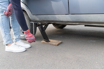 A woman raises a car jack to replace a wheel.