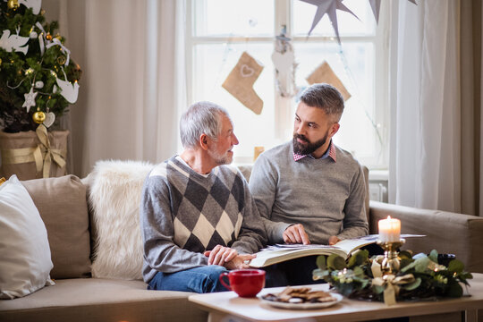Mature man and senior father indoors at home at Christmas, looking at phootgraphs.