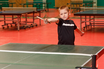 Eight-year-old boy in black T-shirt kicks a ball in table tennis