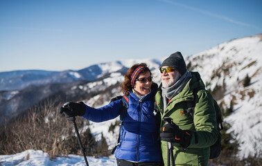 Senior couple hikers with nordic walking poles in snow-covered winter nature.