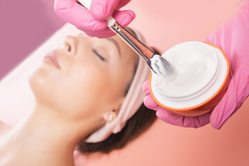 Fototapeta na wymiar Doctor uses anti-aging cream on face of young woman. Spa rejuvenation procedure in salon