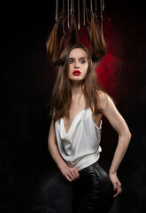 A beautiful girl with evening make-up and red lips wearing a blouse with a deep neckline and her hair suspended on chains, posing on a red and black background. Conceptual, avant-garde design