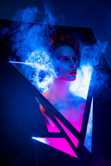 Creative conceptual portrait of a beautiful slim sexy girl with her head thrust into the triangular slots through which smoke and rays of blue and pink light emerge. Artistic, futuristic design