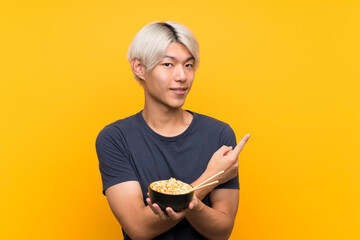 Young asian man over isolated yellow background pointing to the side to present a product