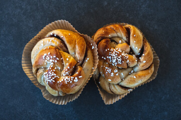 Top down view of two fresh cinnamon buns with sugar on top placed on rustic dark stone table